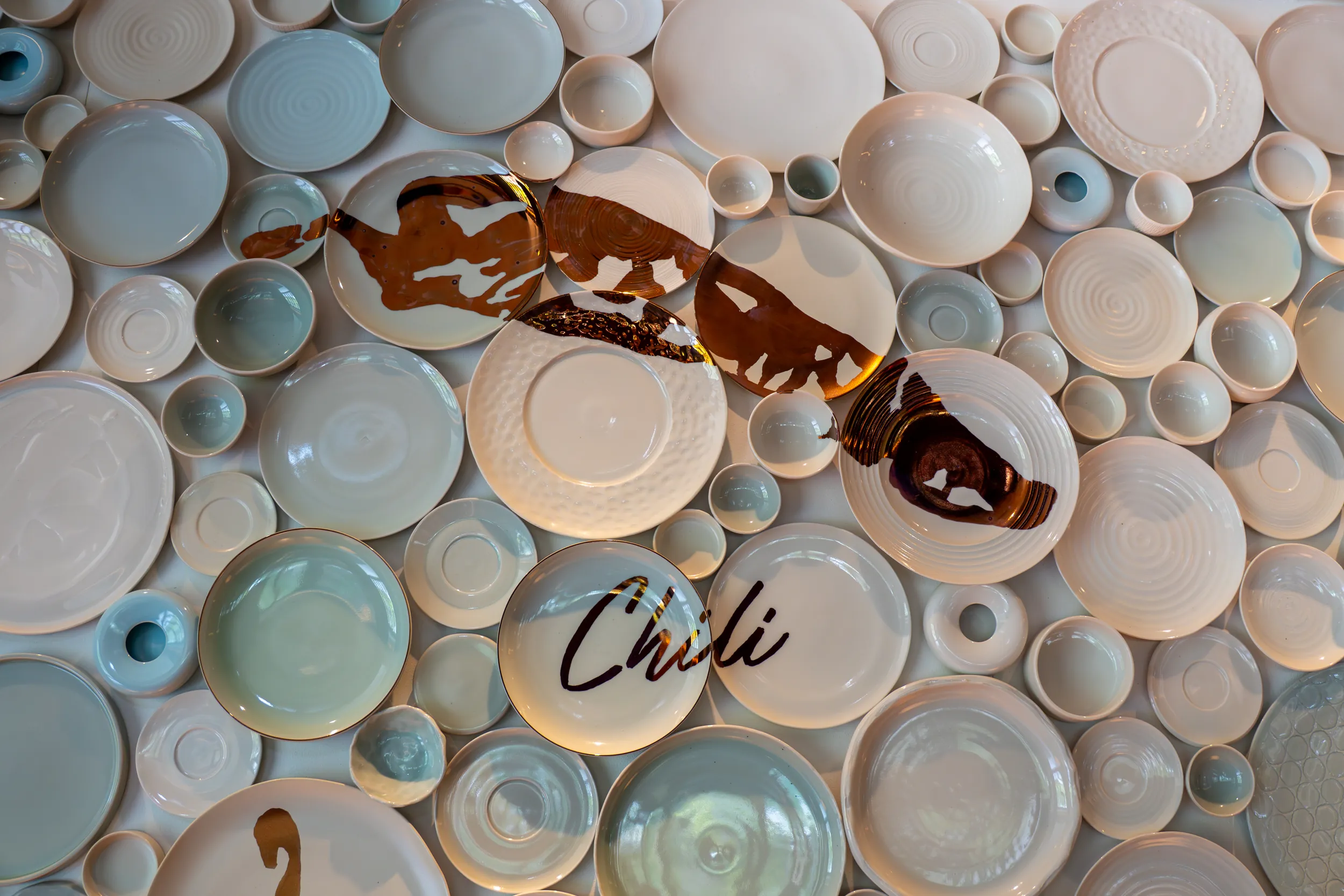 Wall installation of assorted glazed ceramic plates in soft neutral tones
