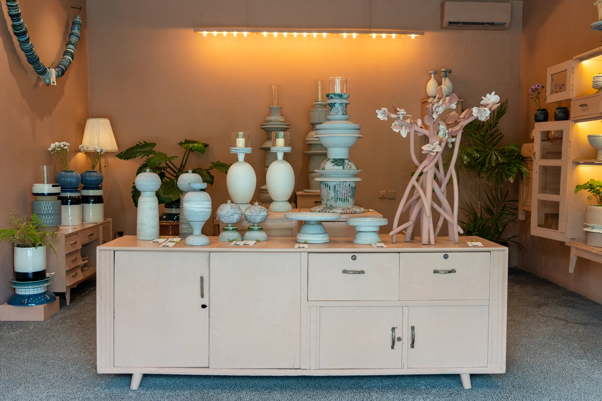 Showroom display of pale ceramic lamps and vases on a cream sideboard