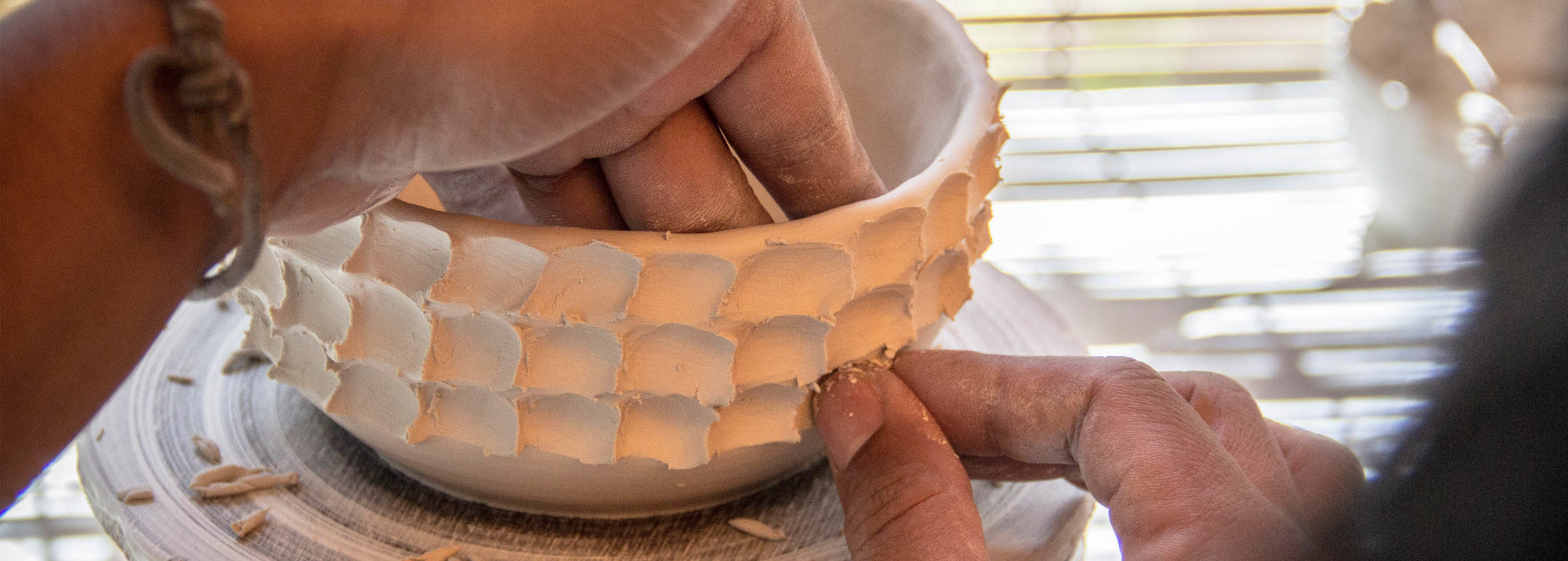 Hands shaping a textured, faceted clay bowl by hand