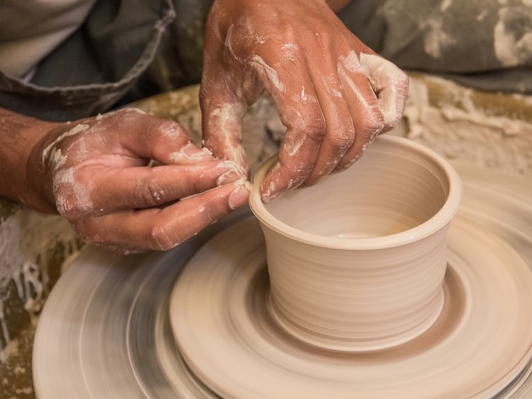 Hands throwing a clay cylinder on the potter's wheel