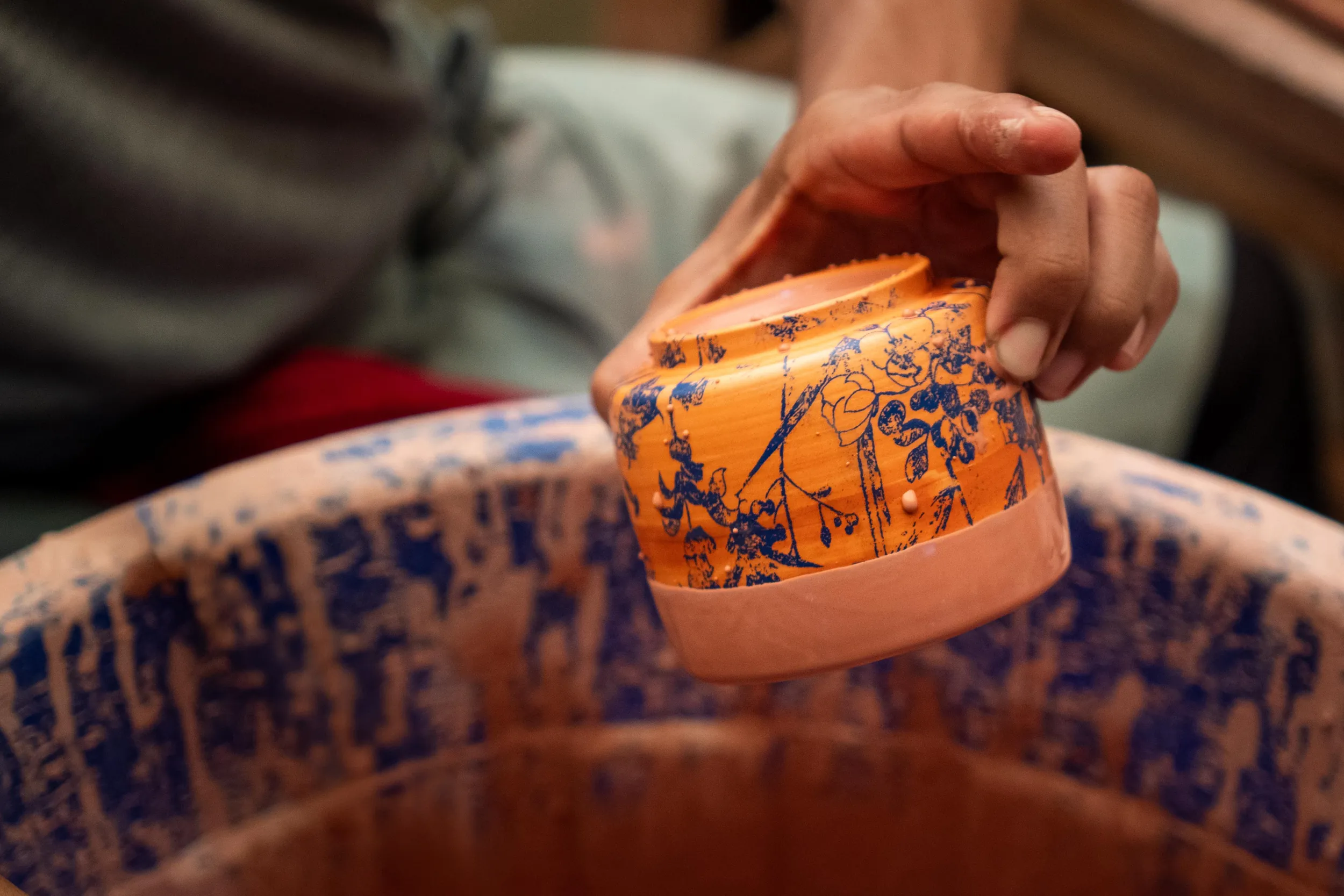 Hands holding a terracotta bowl hand-painted with blue floral decoration