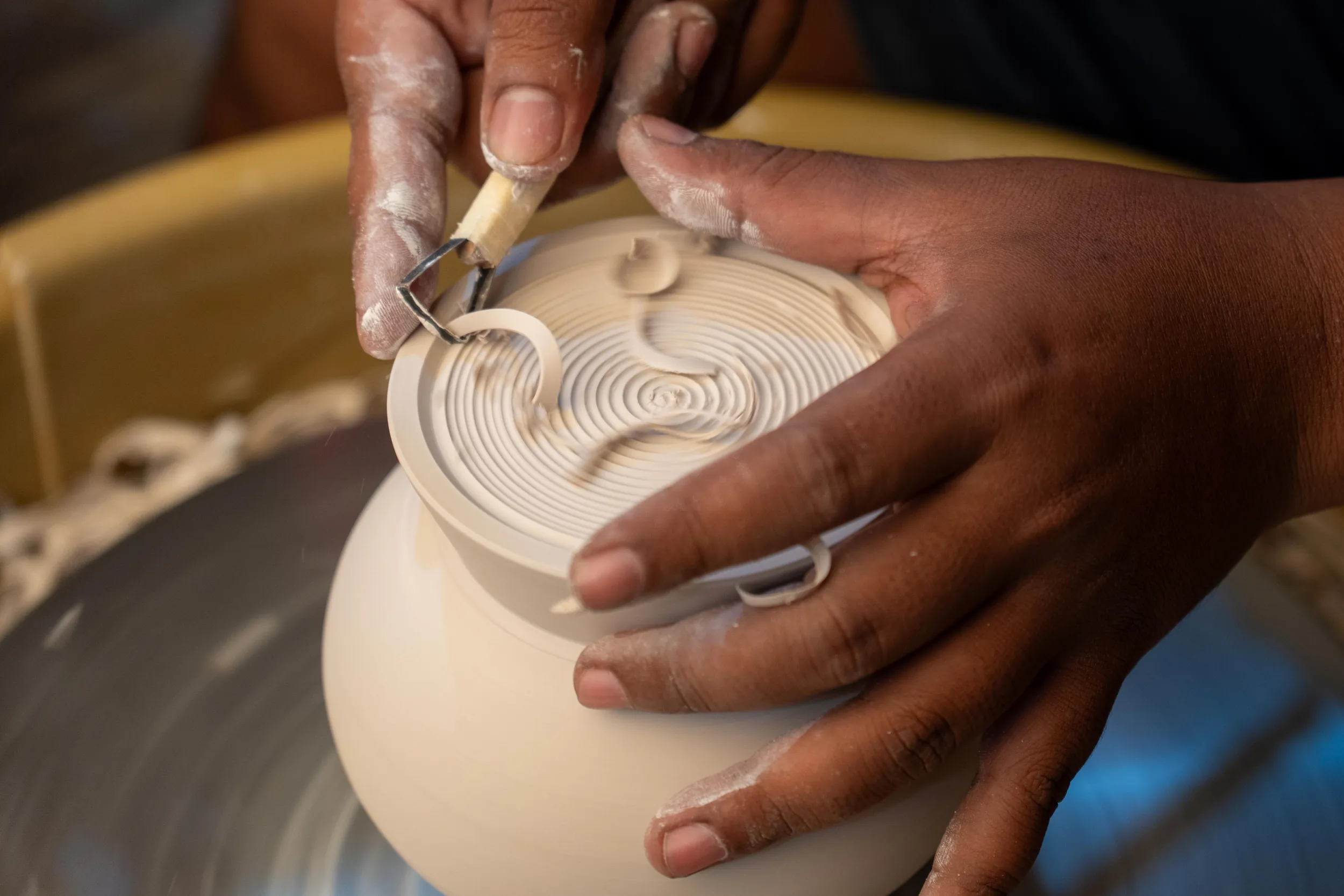 An artisan carving a spiral pattern into a wet clay pot on the wheel