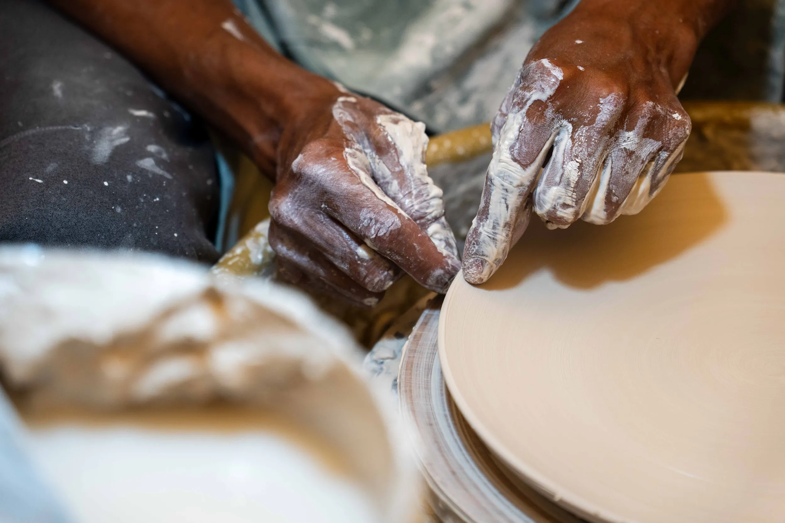 Clay-covered hands shaping a plate on the potter's wheel