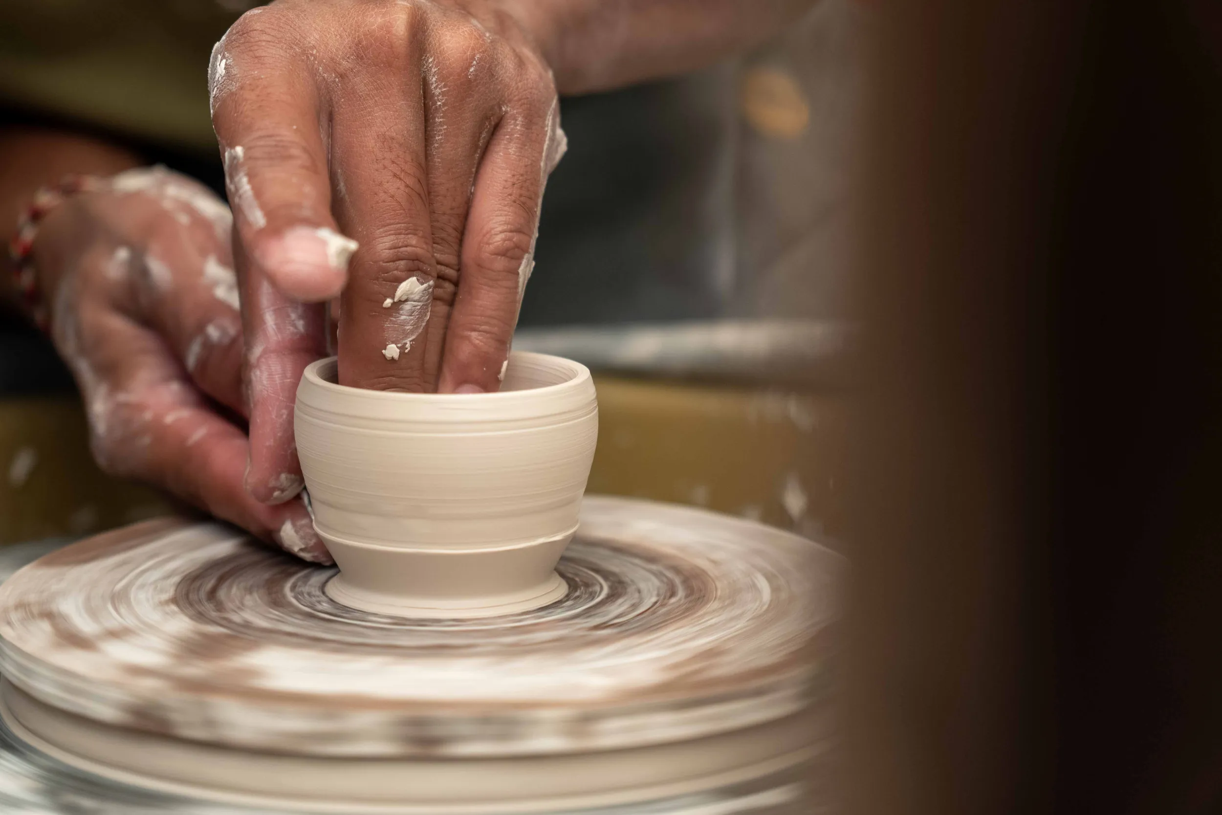Hands throwing a small ceramic cup on the spinning potter's wheel